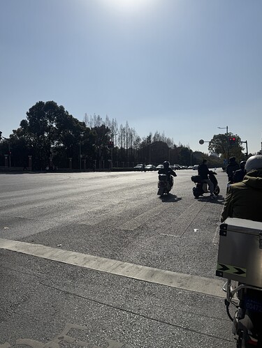 在阳光明媚的日子里,几辆摩托车在马路上等待交通灯,远处可以看到树木和车辆。 #street #vehicles #transportation #trees (由 AI 生成标题)